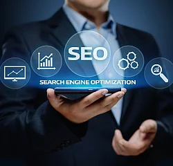 Ein Mann im Anzug hält ein Smartphone, über dem ein holografisches Display schwebt. Darauf steht deutlich SEO und Search Engine Optimization, umgeben von Symbolen für Diagramme, Netzwerke und eine Lupe, die Suchmaschinenoptimierung darstellen.